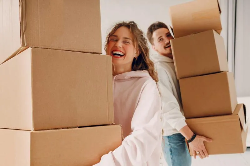Couple carrying labeled moving boxes to storage